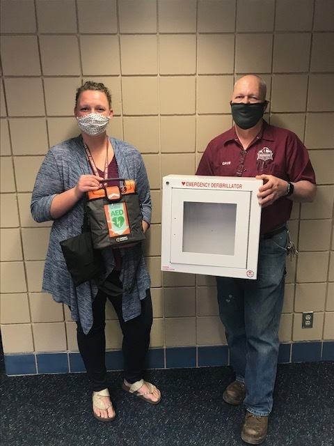 female and male holding an AED and cabinet
