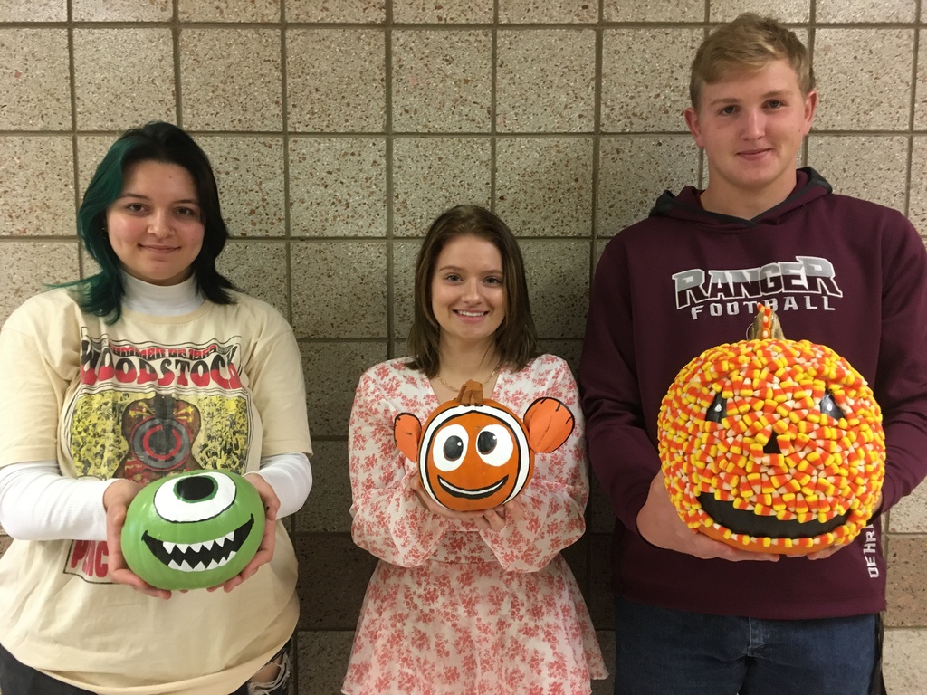 2 female students and 1 male student holding pumpkins
