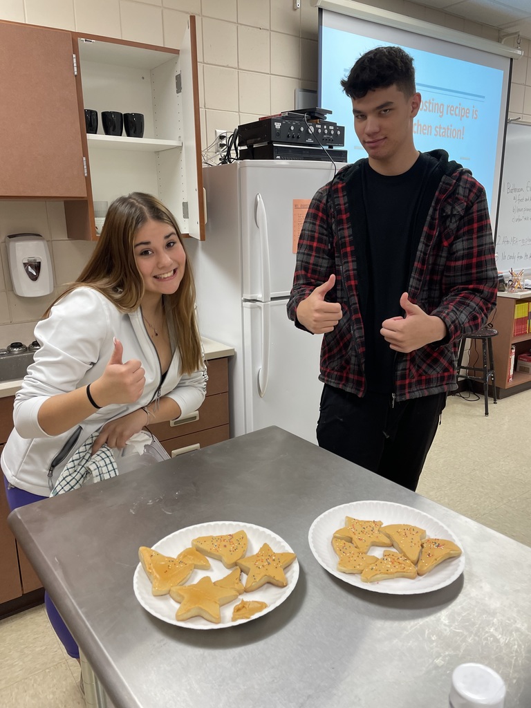 two students giving thumbs up with cookies in front of them