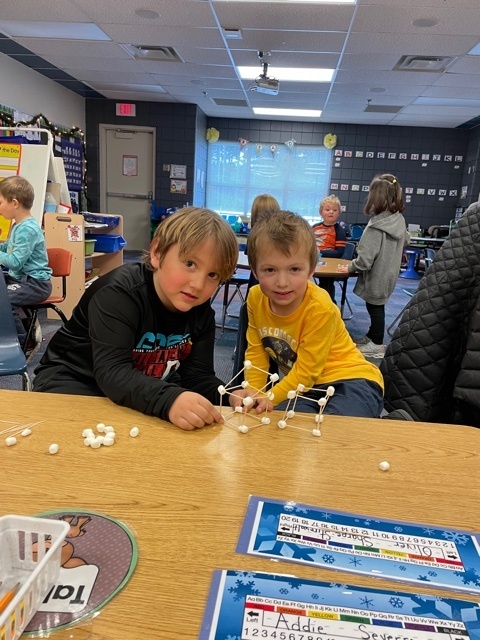 two male students sitting at a desk with marshmallows in front of them