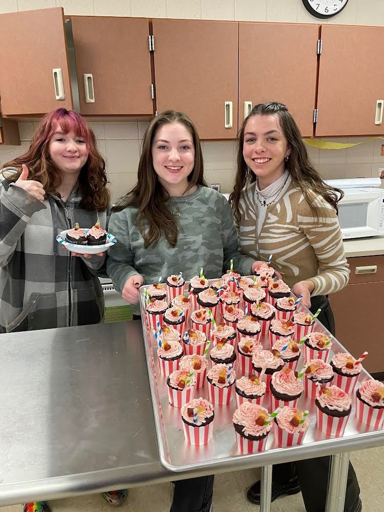 3 students holding a plan of cupcakes 