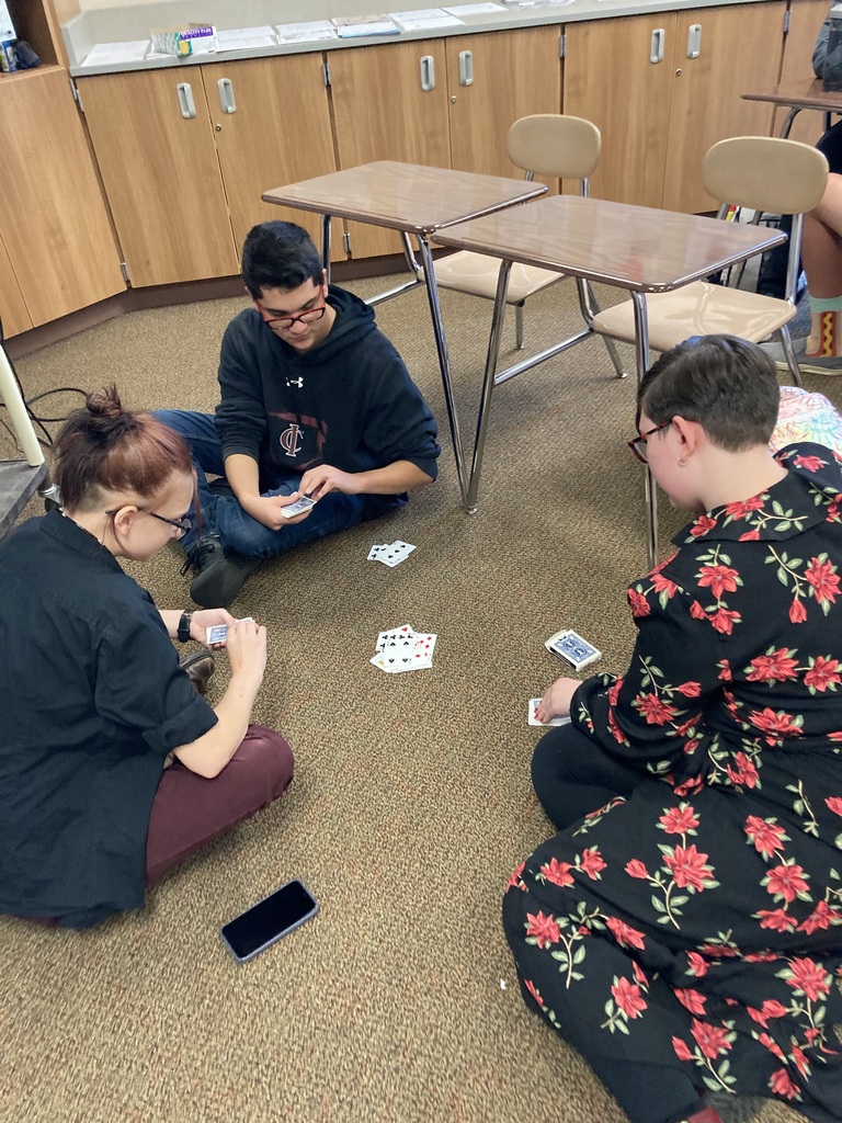 three students playing cards on the floor