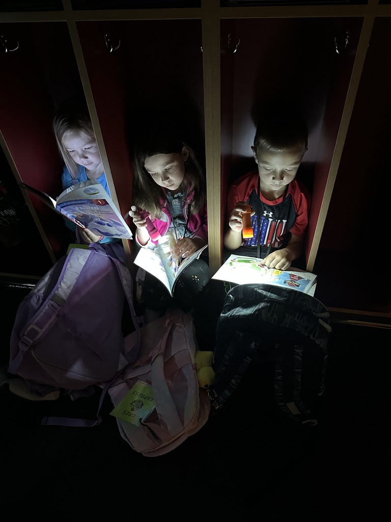 three students reading books with flashlights